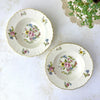 Overhead view of two Syracuse China Portland floral soup bowls with ivory grounds, pink roses, blue and yellow flowers, and gold trim.