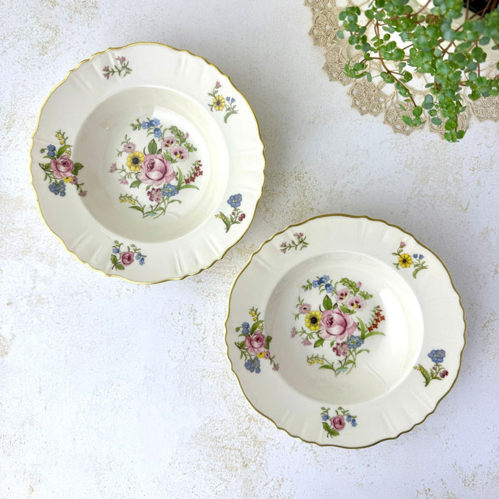 Overhead view of two Syracuse China Portland floral soup bowls with ivory grounds, pink roses, blue and yellow flowers, and gold trim.