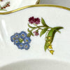 Close-up of a small floral spray with blue, burgundy, pink, and yellow flowers and green leaves on an ivory Syracuse China bowl.