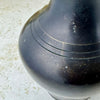 Close-up of blackened brass pitcher showing incised rings, scratches, finish wear, and small areas of exposed brass.