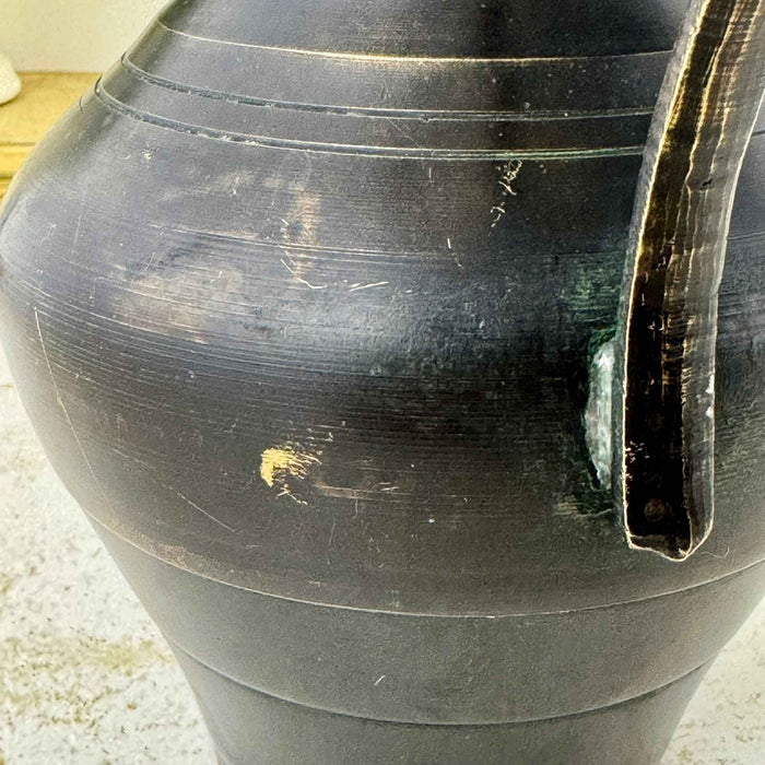 Close-up beside the lower handle attachment showing scratches, finish wear, exposed brass, and green oxidation.