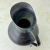 Overhead view into vintage blackened brass pitcher showing the flared pouring lip, dark interior, and curved handle.
