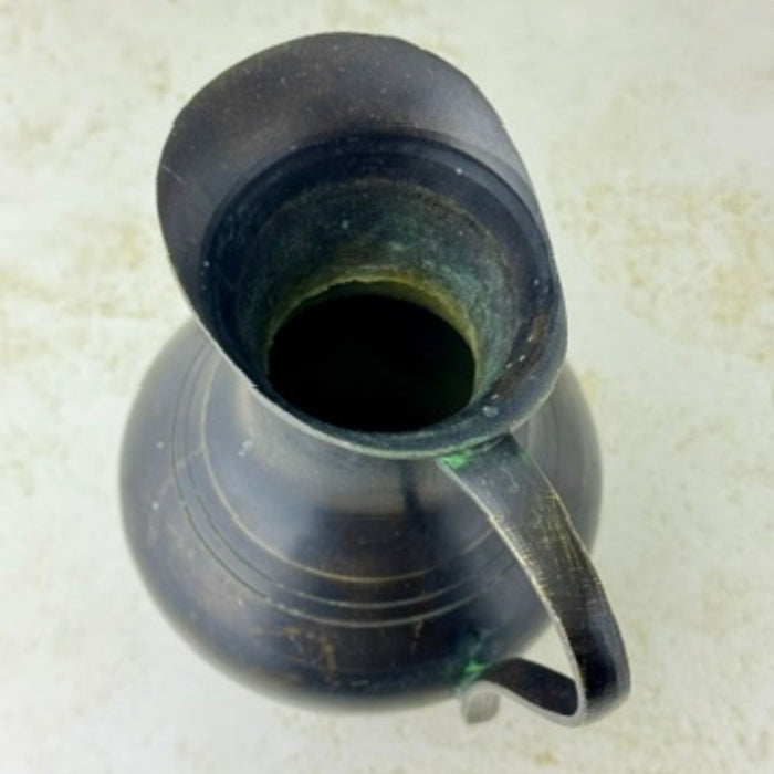 Overhead view into vintage blackened brass pitcher showing the flared pouring lip, dark interior, and curved handle.