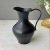 Vintage blackened brass pitcher with rounded body, narrow neck, flared pouring lip, and long curved handle.