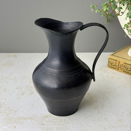 Vintage blackened brass pitcher with rounded body, narrow neck, flared pouring lip, and long curved handle.