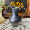 Small vintage blackened brass pitcher styled on a crochet textile in front of a decorative inlaid tray with bird and foliage design.