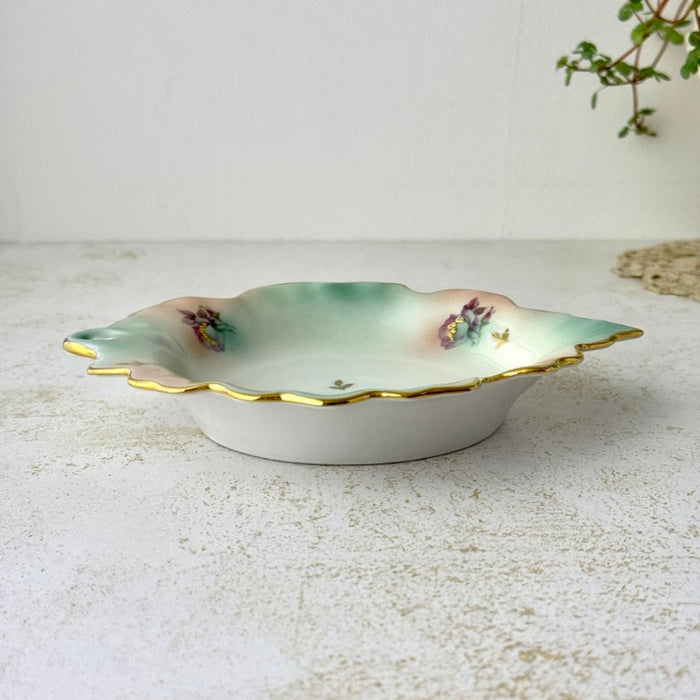 Side view of vintage porcelain trinket dish showing its shallow profile, scalloped gilded edge, and softly shaded interior.