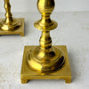 Close-up of the taller brass candlestick showing its turned stem, rounded lower section, and square footed base.