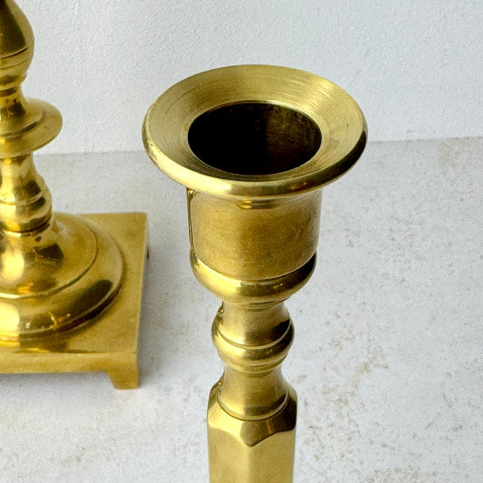 Close-up of the upper section of the shorter brass candlestick showing its flared candle cup, turned stem, and faceted center.