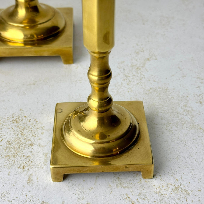 Close-up of the shorter brass candlestick showing its turned lower stem and square footed base.