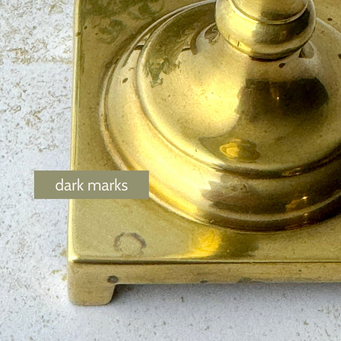 Close-up of dark marks and surface wear on the square base of the shorter vintage brass candlestick.