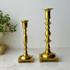 Mismatched pair of vintage solid brass candlesticks with turned stems, square footed bases, and staggered heights.