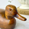 Close-up of the carved wooden duck’s head, elongated bill, visible wood grain, and amber-colored glass eye.