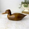 Side view of vintage hand-carved wooden duck showing its long low body, rounded head, pointed tail, and amber-colored glass eye.