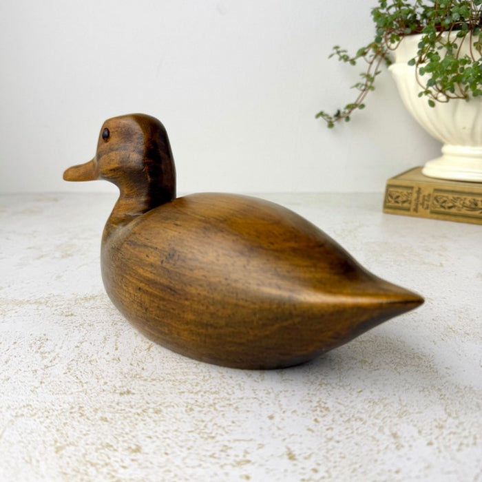 Rear angled view of the carved wooden duck showing its rounded body, tapered pointed tail, and warm brown wood grain.