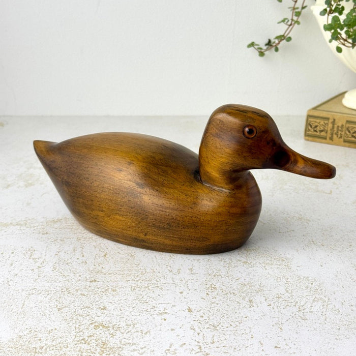 Opposite side view of the vintage wooden duck with elongated bill, smooth rounded body, pointed tail, and glass eye.
