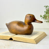 Vintage hand-carved wooden duck with warm brown finish, long low body, elongated bill, and amber-colored glass eyes.