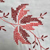 Detailed close-up of cross-stitched leaf embroidery in deep burgundy and coral thread on the cream fabric.