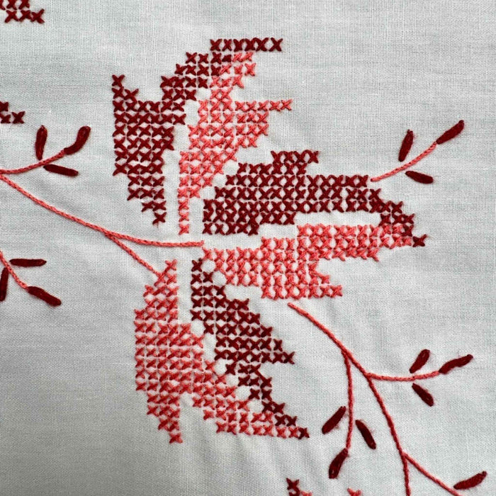 Detailed close-up of cross-stitched leaf embroidery in deep burgundy and coral thread on the cream fabric.