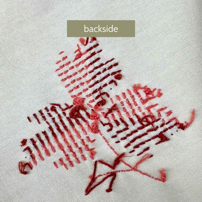 Close-up of the backside of the embroidered leaf motif, showing the burgundy and coral stitching and threadwork.