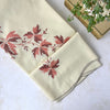 Folded warm cream vintage tablecloth with burgundy and coral embroidered leaves, taupe scalloped edging, books and a green plant.