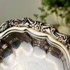 Close-up of ornate raised floral and scroll decoration around the border of the vintage silverplate bowl.