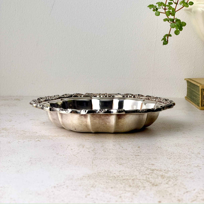 Angled view of vintage silverplate bowl showing its shallow fluted form, reflective interior, and ornate floral border.