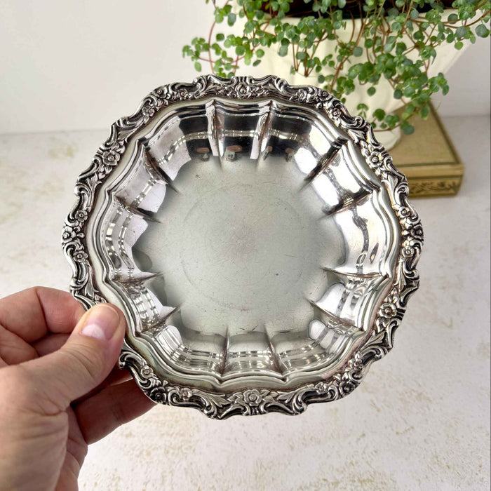 Hand holding up vintage International Silverplate bowl showing the fluted interior and ornate floral and scroll border.