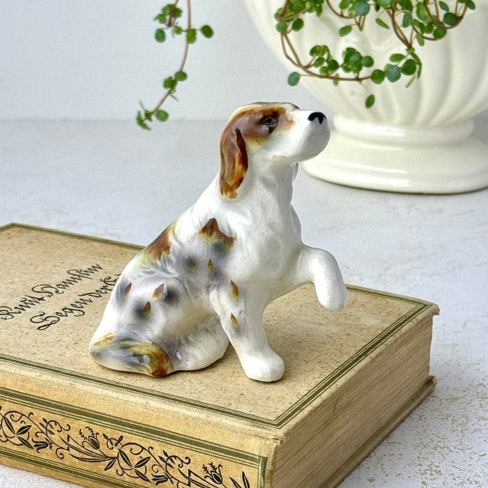 Side view of small ceramic dog figurine with one front paw raised, displayed on a vintage book.