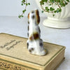 Rear view of ceramic dog figurine showing brown and gray hand-painted markings across the white glazed body.