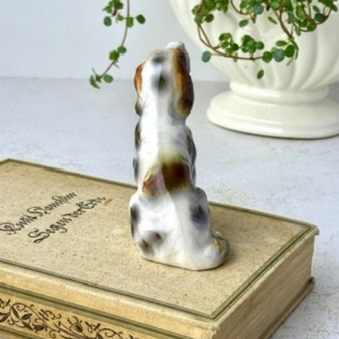 Rear view of ceramic dog figurine showing brown and gray hand-painted markings across the white glazed body.