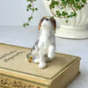 Front view of small ceramic dog figurine seated with one front paw raised.