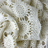 Close view of an ecru crochet table runner gathered in soft folds, showing repeating circular medallions, openwork, and scalloped edging.