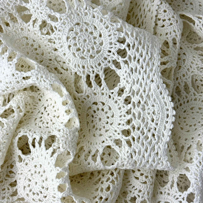 Close view of an ecru crochet table runner gathered in soft folds, showing repeating circular medallions, openwork, and scalloped edging.