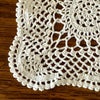 Close view of the rounded corner and scalloped edging of an ecru crochet table runner against a dark wood surface.
