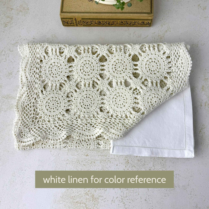Folded ecru crochet table runner shown beside a white linen for color comparison, with circular medallions and openwork visible.
