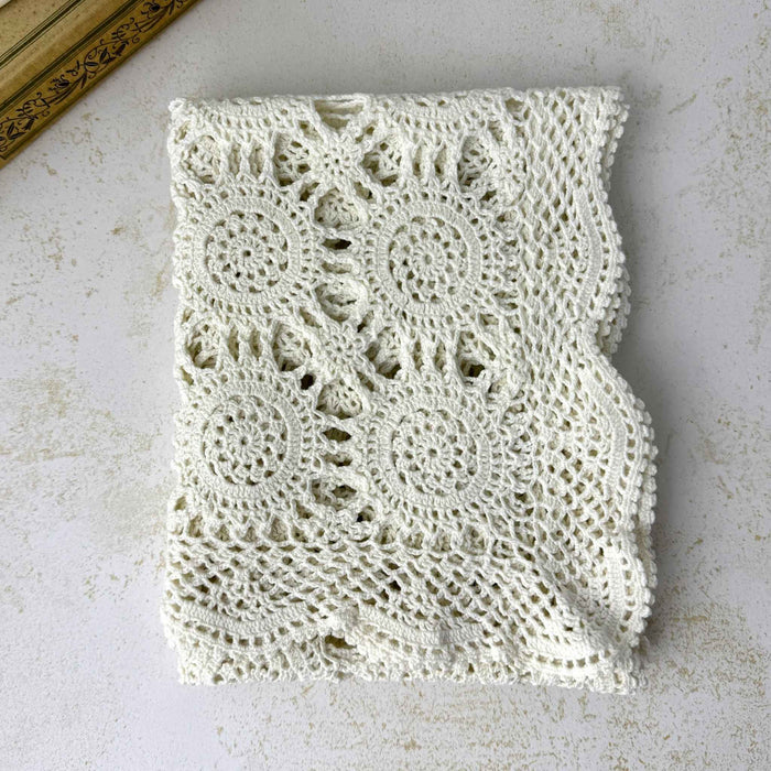Overhead view of a neatly folded ecru crochet table runner showing repeating circular medallions, openwork, and scalloped edges.