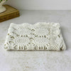 Low-angle view of a folded ecru crochet table runner showing layered openwork, circular medallions, and scalloped edging.
