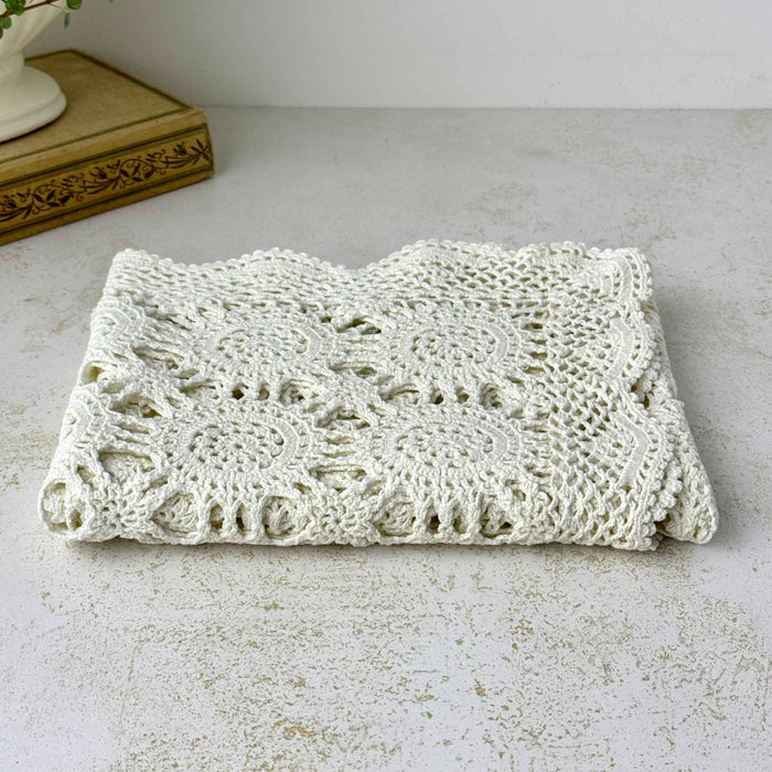 Low-angle view of a folded ecru crochet table runner showing layered openwork, circular medallions, and scalloped edging.