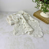 Ecru crochet table runner loosely draped on a light surface beside a decorative book and white planter with trailing greenery.