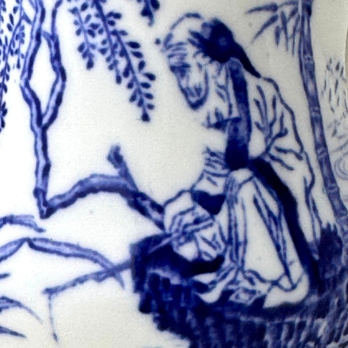 Close-up of Blue Mikado decoration showing a seated man fishing beside the water amid trees and landscape.