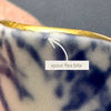 Close-up of the creamer spout showing the tiny flea bite just below the gold-trimmed rim.