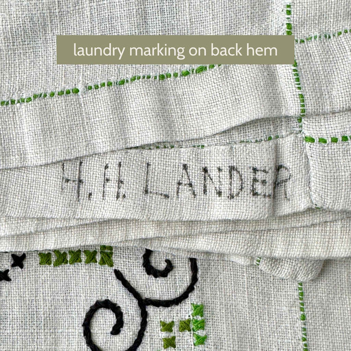 Back hem of the ecru embroidered tablecloth showing a faded handwritten laundry marking in dark ink.