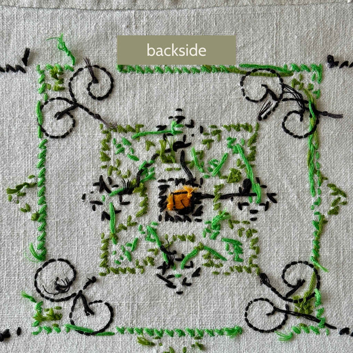 Backside of an embroidered medallion showing the reverse stitching and numerous loose thread ends in green and navy.
