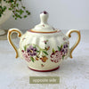 Opposite side of sugar bowl showing hand-painted floral decoration, ribbed body, and two curved handles.