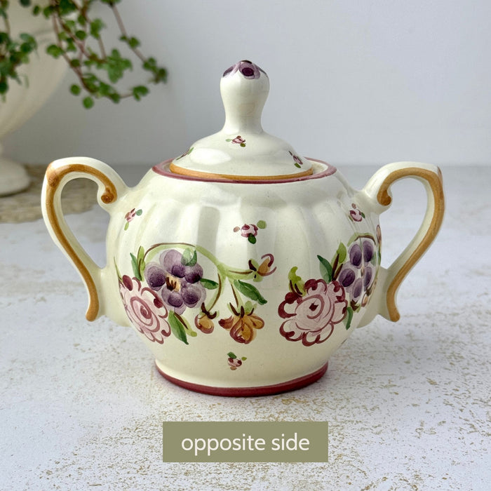 Opposite side of sugar bowl showing hand-painted floral decoration, ribbed body, and two curved handles.