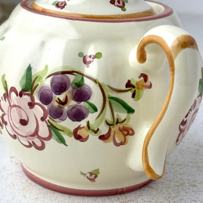 Close-up of sugar bowl showing loosely painted purple and pink flowers, green leaves, and golden brown handle decoration.