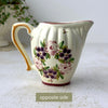 Opposite side of ceramic creamer showing floral decoration, ribbed body, and curved pouring spout.