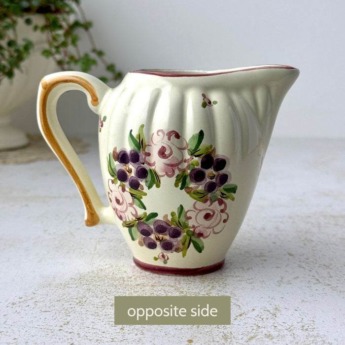 Opposite side of ceramic creamer showing floral decoration, ribbed body, and curved pouring spout.