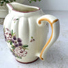 Close-up of creamer showing golden brown painted handle, cream glaze, and part of the floral decoration.